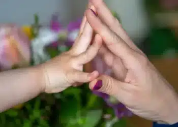 Mãe e filho realizando um gesto de afeto, com flores ao fundo, representando o carinho e a conexão.