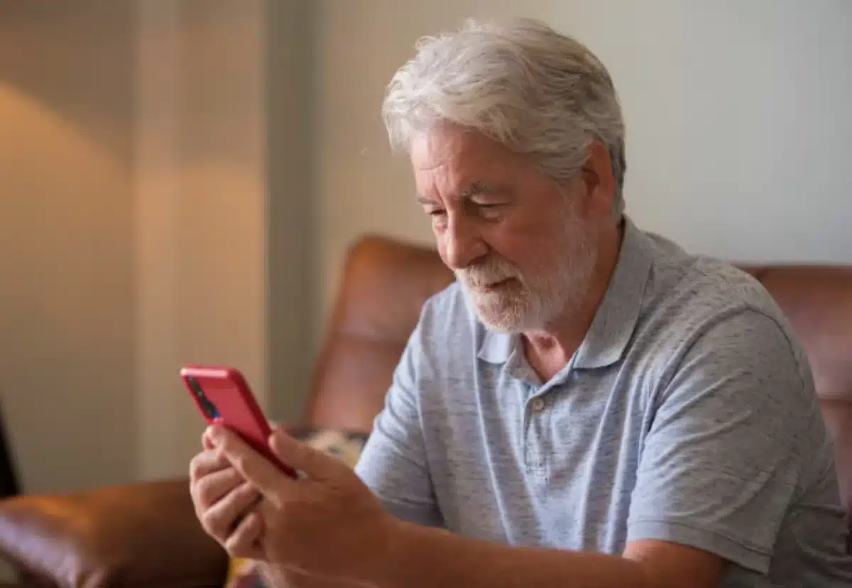 Veja o que você precisa fazer para se proteger de golpes e fraudes Homem idoso usando celular com atenção, representando cuidados ao navegar na internet.