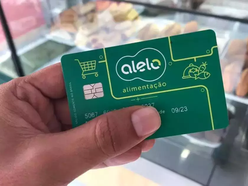 Cartão Alelo alimentação. Cartão Alelo Alimentação sendo segurado por uma pessoa, destacando a bandeira do vale-alimentação.