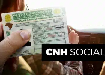 A mão de uma pessoa segurando a CNH, Carteira Nacional de Habilitação, com o volante e o painel de um carro ao fundo. A imagem ilustra o benefício do programa CNH Social.