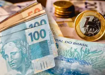 Mão segurando um cartão de benefício social com notas de dinheiro, simbolizando a ajuda financeira.
