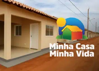 Fachada de casas populares novas e idênticas de um condomínio do programa Minha Casa, Minha Vida, ao lado do logotipo oficial.