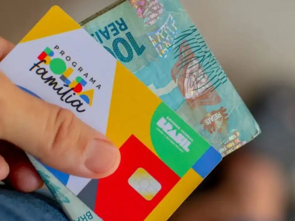 Quem recebe o Bolsa Família em setembro de 2025. Cartão do Bolsa Família sendo segurado junto com cédula de cem reais, simbolizando pagamento do benefício