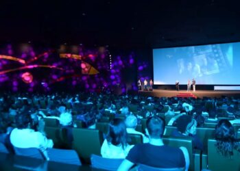 Grande público em uma sala de cinema ou teatro assistindo a uma apresentação no palco, ilustrando o tipo de evento (cultural ou show) onde os beneficiários do Bolsa Família podem ter direito ao desconto da meia-entrada.