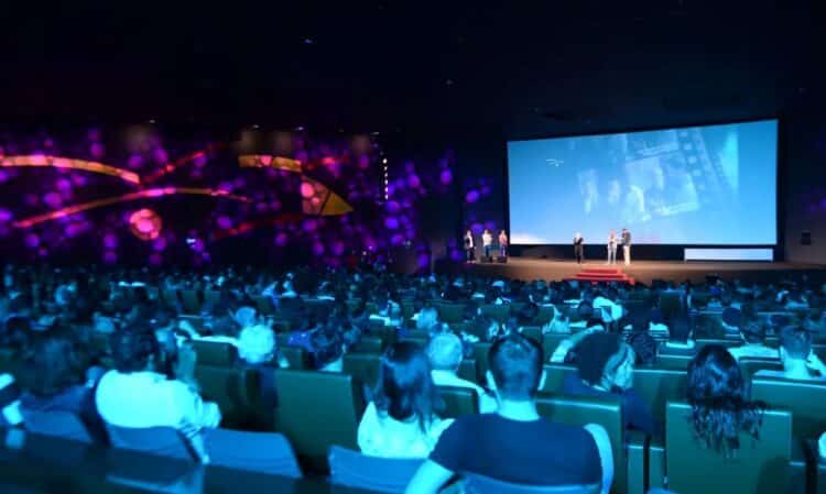 Grande público em uma sala de cinema ou teatro assistindo a uma apresentação no palco, ilustrando o tipo de evento (cultural ou show) onde os beneficiários do Bolsa Família podem ter direito ao desconto da meia-entrada.
