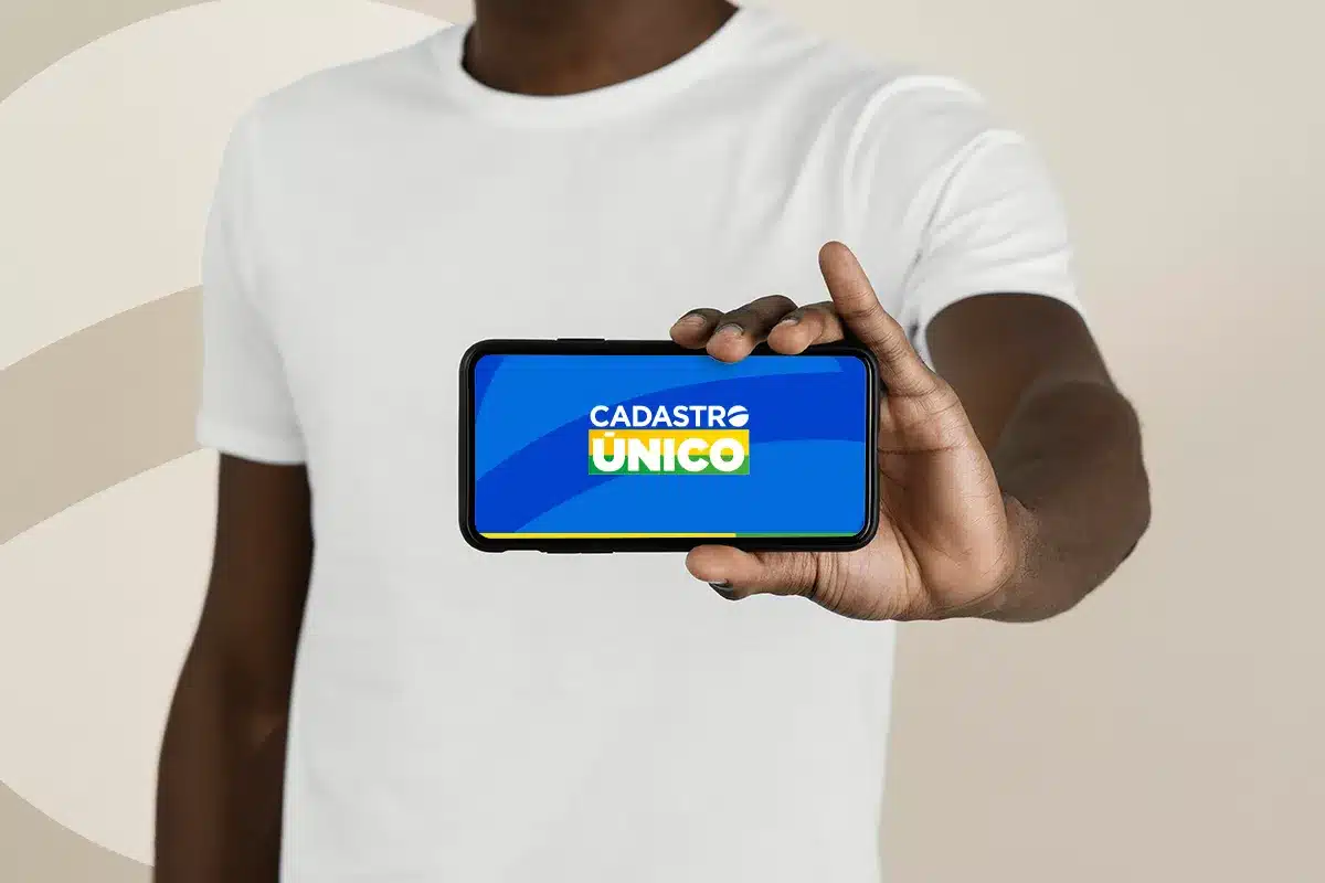 Cadastro Único - Oportunidades Jovens 2025 Homem segurando um smartphone que exibe o logotipo do Cadastro Único, representando o ponto de partida para jovens buscarem informações e oportunidades.