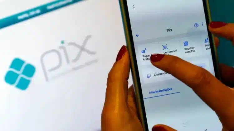 Pix por foto: aprenda a usar a função do Banco do Brasil 1 Mão feminina segurando um smartphone com a tela do aplicativo Pix aberta, mostrando opções de pagamento e leitura de QR Code, com a logo Pix ao fundo, ilustrando a função Pix por foto.