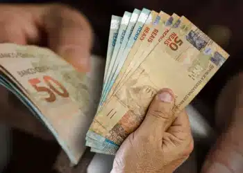 Mãos segurando várias cédulas de real brasileiro em diferentes valores.