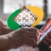 Quer saber quanto tempo falta para se aposentar? Calculadora do INSS te ajuda 11 Mãos de idoso segurando e usando um smartphone em ambiente interno com logo da Previdência Social