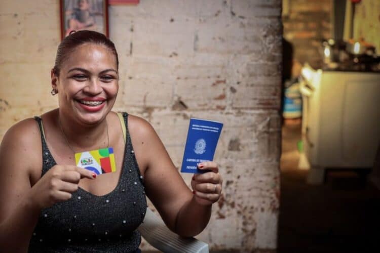 Mulher sorridente segura o cartão do Bolsa Família e uma Carteira de Trabalho, simbolizando a união do benefício social com a inserção profissional feminina.