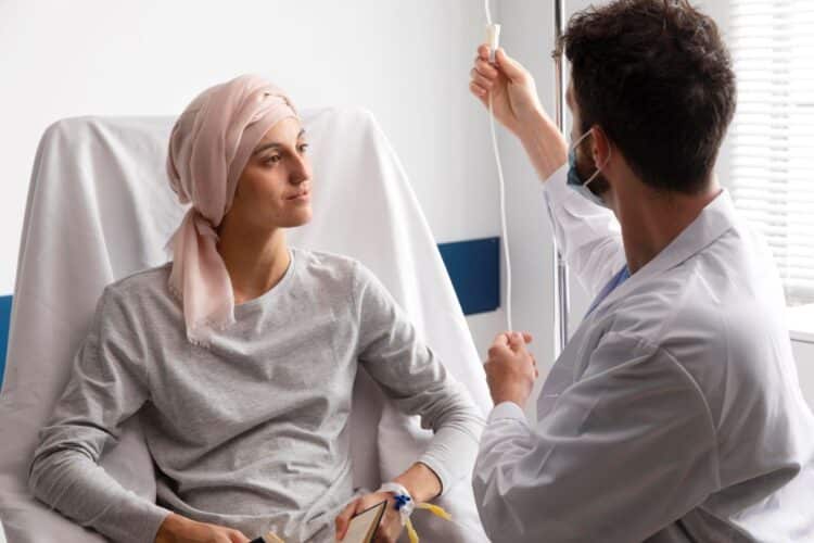 Profissional de saúde ajustando soro em paciente submetida à radioterapia, simbolizando o suporte oferecido pelo novo auxílio.
