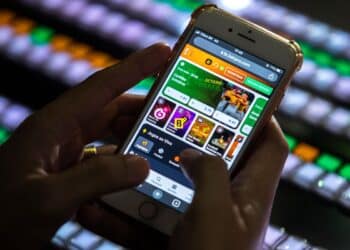 Pessoa usando um celular para acessar uma casa de apostas online, ilustrando a proibição e o bloqueio de pagamentos do Bolsa Família em sites de apostas e jogos.