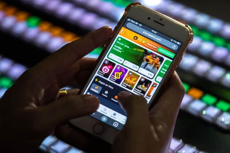 Pessoa usando um celular para acessar uma casa de apostas online, ilustrando a proibição e o bloqueio de pagamentos do Bolsa Família em sites de apostas e jogos.
