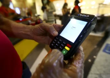 Prefeitura lança vale-alimentação no valor de R$ 200 para famílias carentes 5 Mãos usando máquina de cartão Cielo para realizar pagamento em ambiente interno