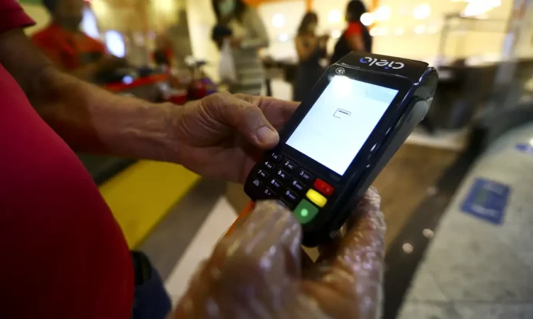 Mãos usando máquina de cartão Cielo para realizar pagamento em ambiente interno