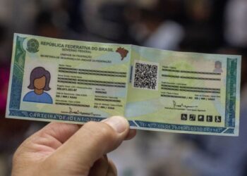 Uma mão segura a Nova Carteira de Identidade Nacional (CIN) verde e amarela com dados genéricos e um QR Code visível. Documento usado para ilustrar o mutirão do SAC para crianças e adolescentes.