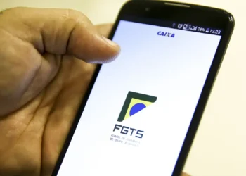 Imagem de uma mão segurando um celular e na tela está escrito FGTS
