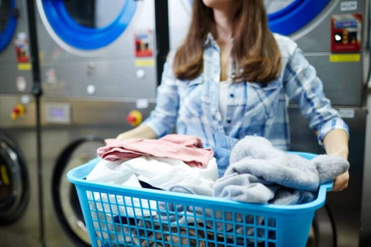 Mulher segura cesto de roupas em lavanderia, simbolizando a iniciativa do governo para aliviar a carga doméstica feminina.