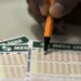 Vendas liberadas! Você já pode apostar na Mega Sena da Virada 2025; saiba como jogar 11 Mão segurando caneta laranja preenchendo volante da Mega-Sena com números marcados