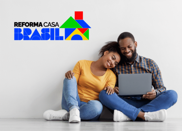 Casal feliz sentado no chão, usando um laptop, com o logotipo "Reforma Casa Brasil" ao fundo, representando acesso a programas habitacionais.