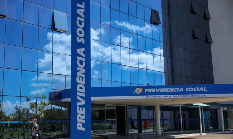 Fachada moderna e espelhada da sede do Instituto Nacional do Seguro Social (INSS), com o pilar azul vertical escrito "PREVIDÊNCIA SOCIAL" em letras grandes, indicando o local para solicitar a devolução de valores descontados indevidamente.