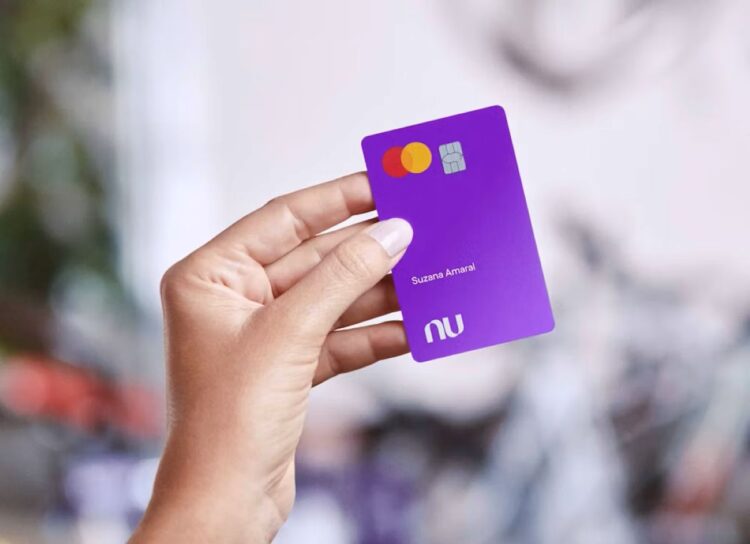 Mão segurando um cartão Nubank roxo, com o nome 'Suzana Amaral', simbolizando o benefício de 50% de desconto na Shopee para clientes.