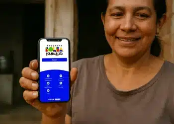 Mulher segurando um celular com a tela do aplicativo do Bolsa Família, mostrando opções como calendário de pagamentos e informações sobre o programa.