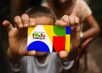 Mão de criança segurando cartão colorido do Programa Bolsa Família com formas geométricas coloridas