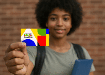 Jovem segurando o cartão moderno do Programa Bolsa Família, simbolizando o recebimento e o uso do benefício. O cartão é colorido, com fundo de tijolos desfocado.