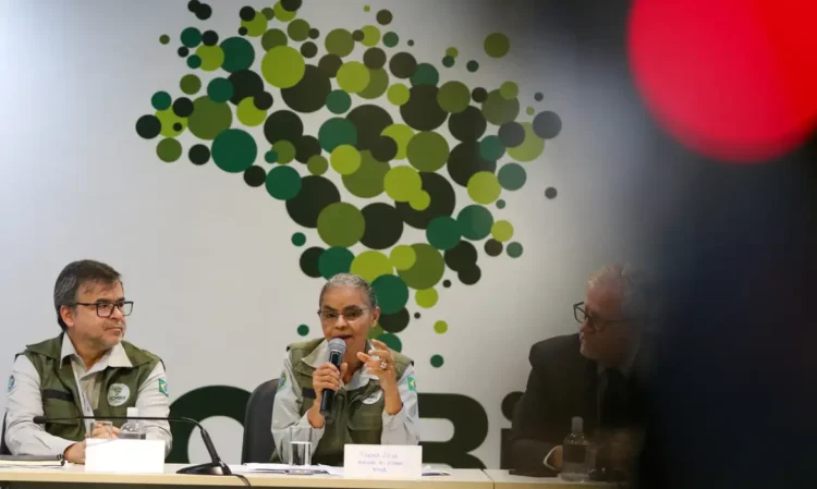 Bolsa Verde de R$600: Programa ajuda famílias que protegem o meio ambiente 1 Pessoas em reunião formal do ICMBio com microfone e mural de círculos verdes ao fundo