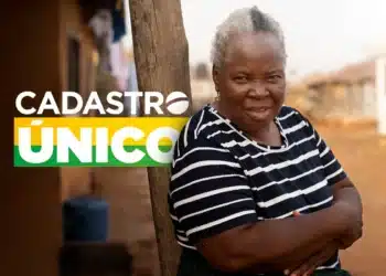 Mulher idosa sorridente com camisa listrada em área rural junto ao texto Cadastro Único ao fundo