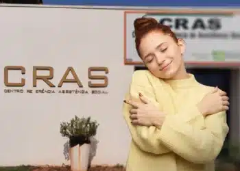 CRAS emite comunicado oficial sobre atendimentos para esta terça-feira (18) 9 Mulher sorrindo e abraçando a si mesma em frente a unidade do CRAS, representando acolhimento nos atendimentos.