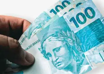 Salário Mínimo 2026: Mão segurando cédulas de R$ 100 Reais, ilustrando a preocupação e o impacto financeiro das mudanças previstas para o novo valor do salário mínimo em 2026.