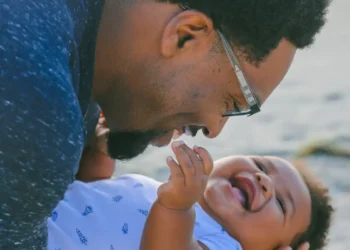 Pai de óculos sorrindo enquanto segura e brinca com bebê que ri muito