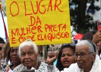 Pessoas em protesto segurando placa amarela com frase sobre lugar da mulher preta