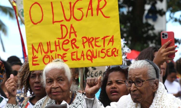 Pessoas em protesto segurando placa amarela com frase sobre lugar da mulher preta