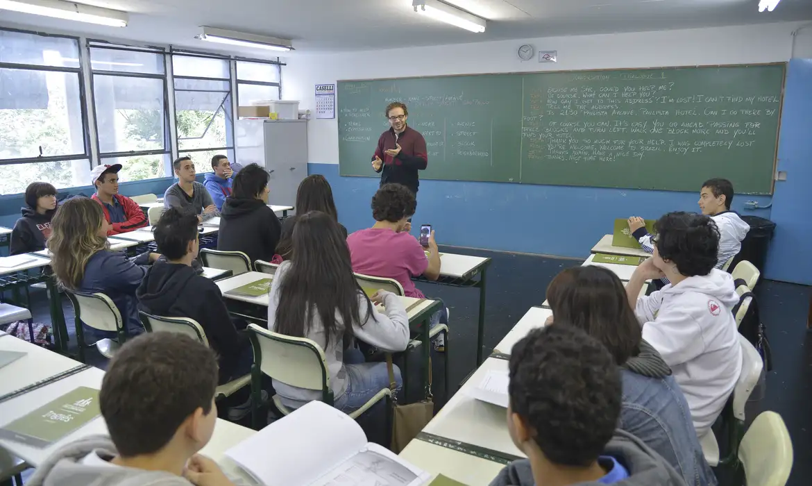 Sala de aula com professor e alunos em aula Professor ministrando aula para turma de estudantes sentados em carteiras de sala de aula