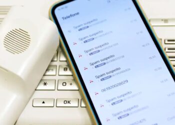Tela de celular mostrando várias chamadas identificadas como spam suspeito ao lado de telefone fixo branco.