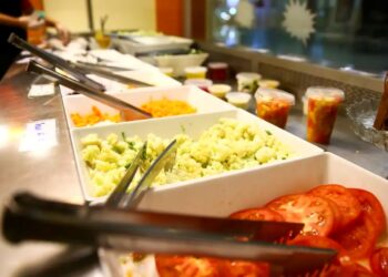 Buffet de restaurante com travessas de saladas, tomates e couve-flor, representando o uso do vale-refeição após as atualizações na legislação de benefícios em 2026.