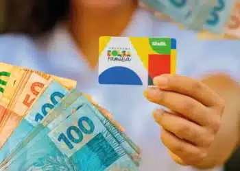 Pessoa segurando cartão do Programa Bolsa Família com cédulas de real em destaque