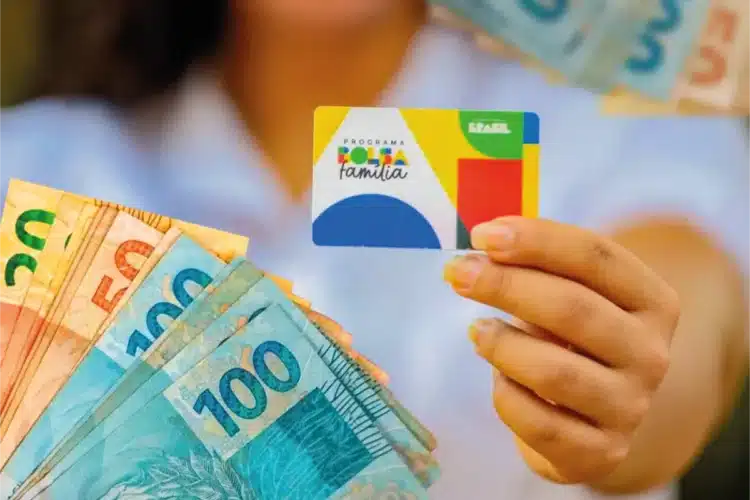 Pessoa segurando cartão do Programa Bolsa Família com cédulas de real em destaque
