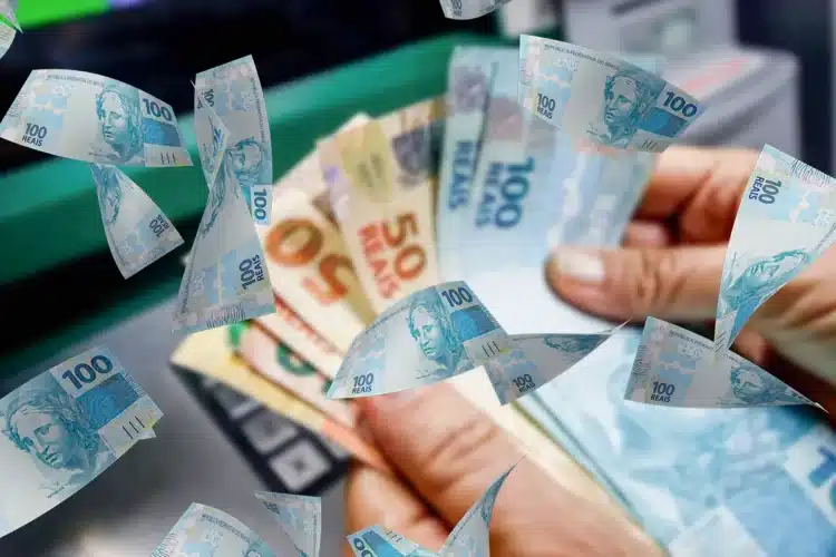 Mãos segurando diversas cédulas de reais com notas de 50 e 100 reais, dinheiro voando ao redor