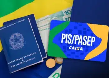 Saiu o calendário do PIS/PASEP 2026: Confira seu mês de pagamento 10 Carteira de trabalho, dinheiro em reais e cartão PIS/PASEP Caixa sobre bandeira do Brasil
