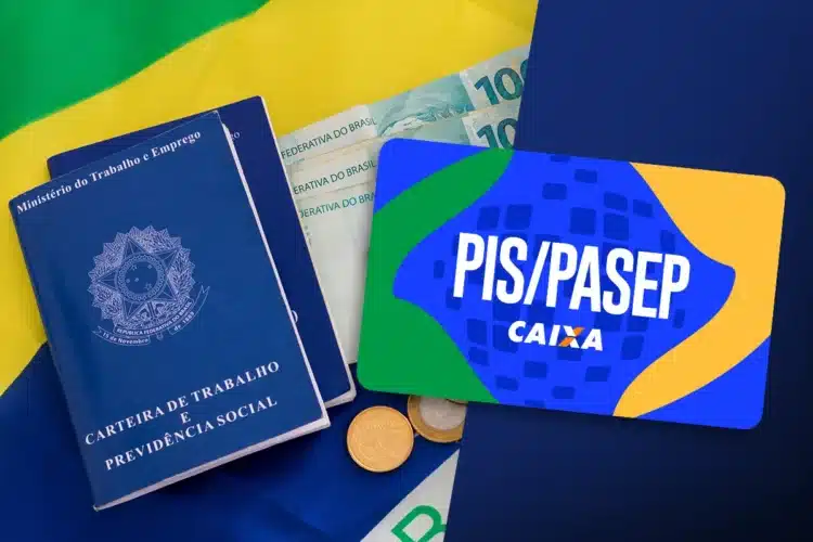 Saiu o calendário do PIS/PASEP 2026: Confira seu mês de pagamento 1 Carteira de trabalho, dinheiro em reais e cartão PIS/PASEP Caixa sobre bandeira do Brasil