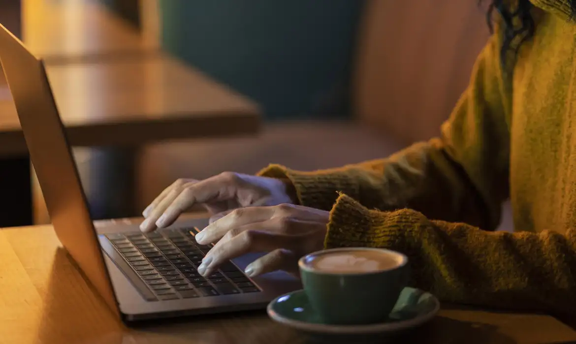 Trabalho remoto no conforto com laptop e café Pessoa digitando no laptop acompanhado por uma xícara de café em ambiente aconchegante