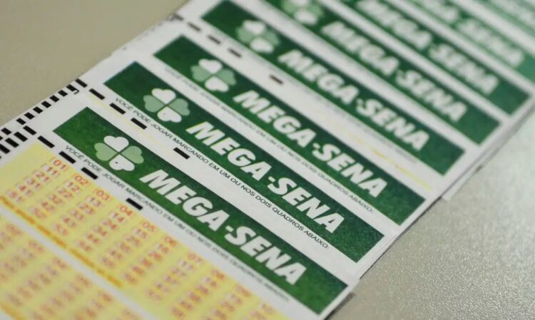Close-up inclinado de vários volantes de aposta da Mega-Sena empilhados, mostrando o logotipo verde e os campos de números para marcação.