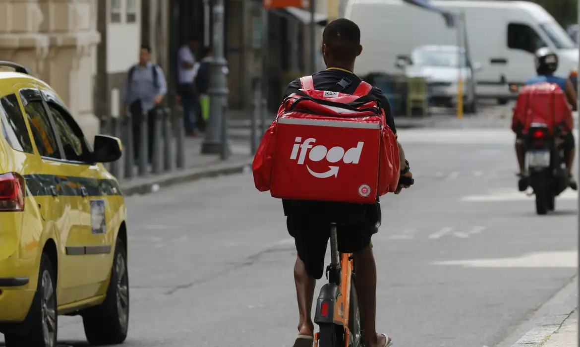 Entregador de Destaque: O Caminho para o Bônus do Programa iFood Super. Entregador de bicicleta do iFood pedalando na rua, representando os profissionais que buscam alto desempenho para participar do programa de premiação Super.