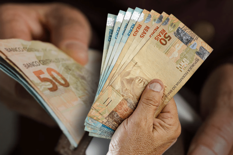 Mãos segurando notas de 50 reais, representando o pagamento do 13º salário.