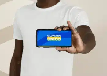 Pessoa segura celular exibindo tela do Cadastro Único, referência aos benefícios sociais
