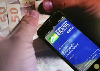 Aplicativo Auxílio Emergencial Caixa com nota de cinquenta reais ao fundo.